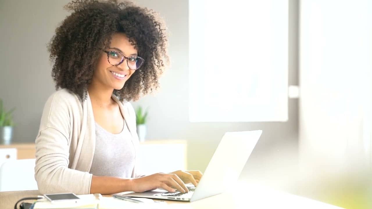 Smiling employee using laptop in a modern, bright office space.
