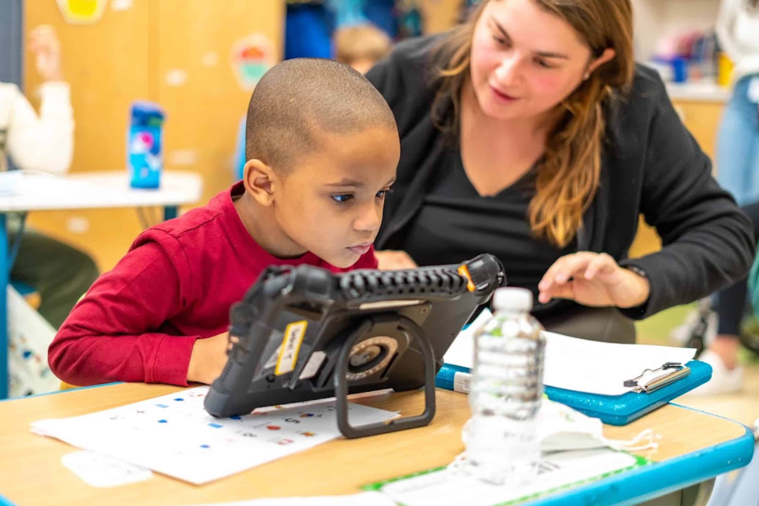Boy with hearing aid engaged in learning with teacher in classroom.