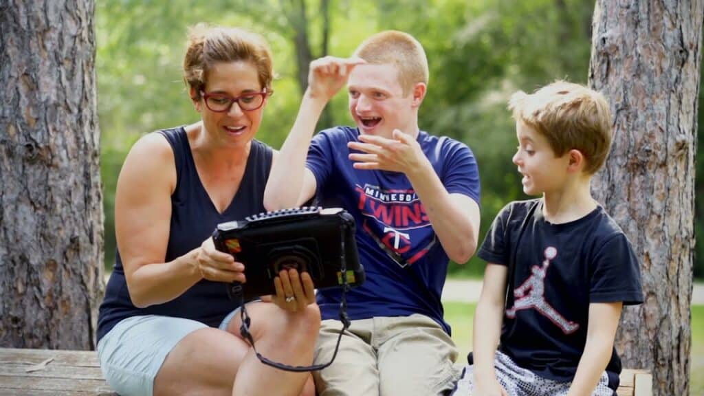 Tyler explores communication with family using a speech-generating device outdoors.