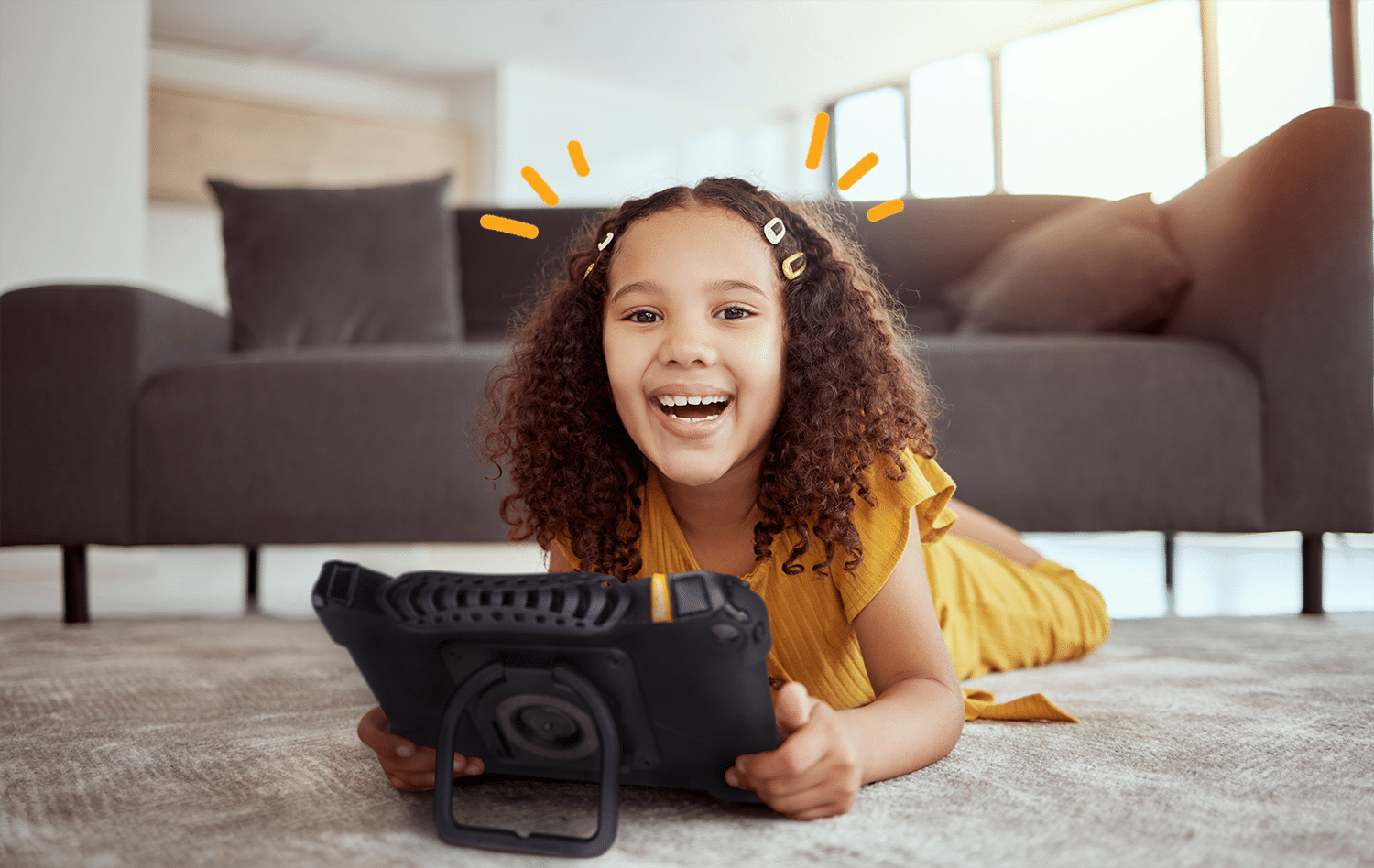A joyful girl playing with a tablet on the floor in a cozy living room.