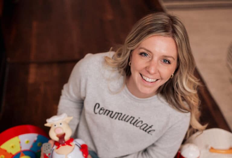 Smiling woman surrounded by colorful toys in a playful, joyful setting.