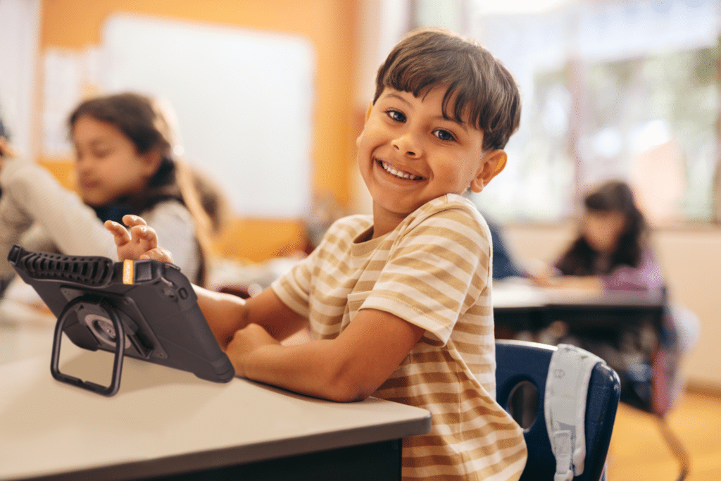 Happy child engaged in learning with a tablet in a classroom setting.
