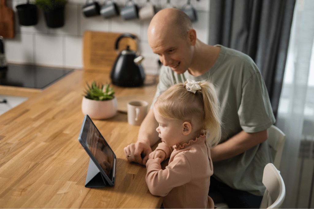 Dad and daughter enjoy quality time watching a tablet together during a teletherapy session at home.