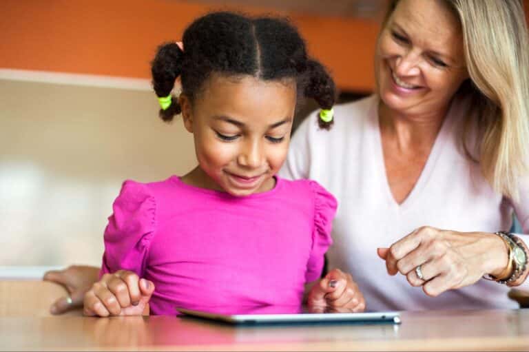 Child excitedly learns with a tablet alongside a caring adult.