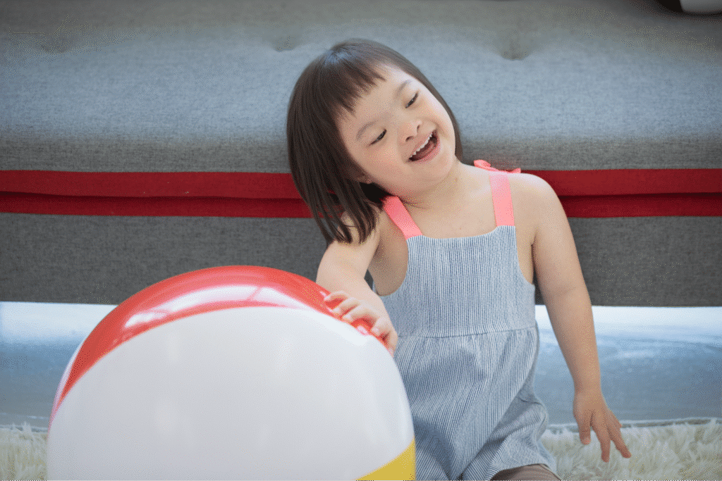 Happy down syndrome child enjoying playtime with a colorful beach ball indoors.