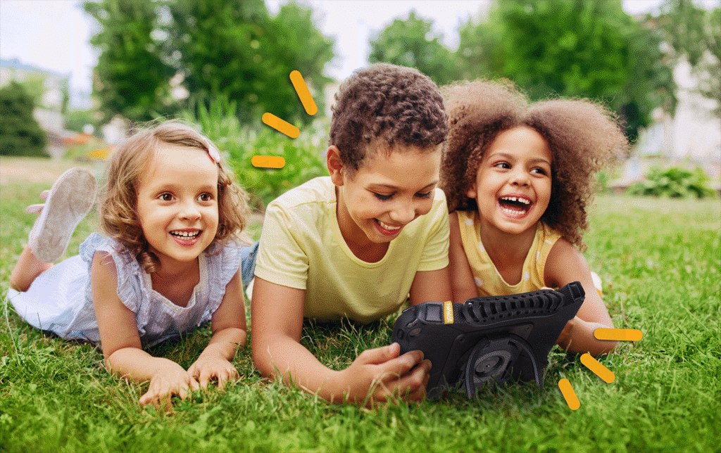 Kids enjoying fun outdoor playtime in grass while using a tablet together.