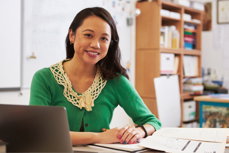 Inspiring teacher smiling in a colorful classroom, promoting a positive learning environment.