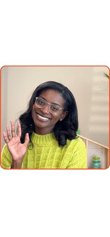 Smiling woman in a green sweater waves cheerfully at the camera.