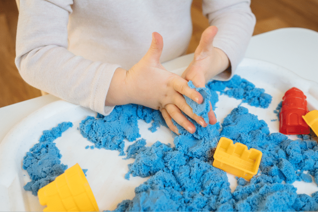 Child enjoying creative play with blue kinetic sand and colorful toys.