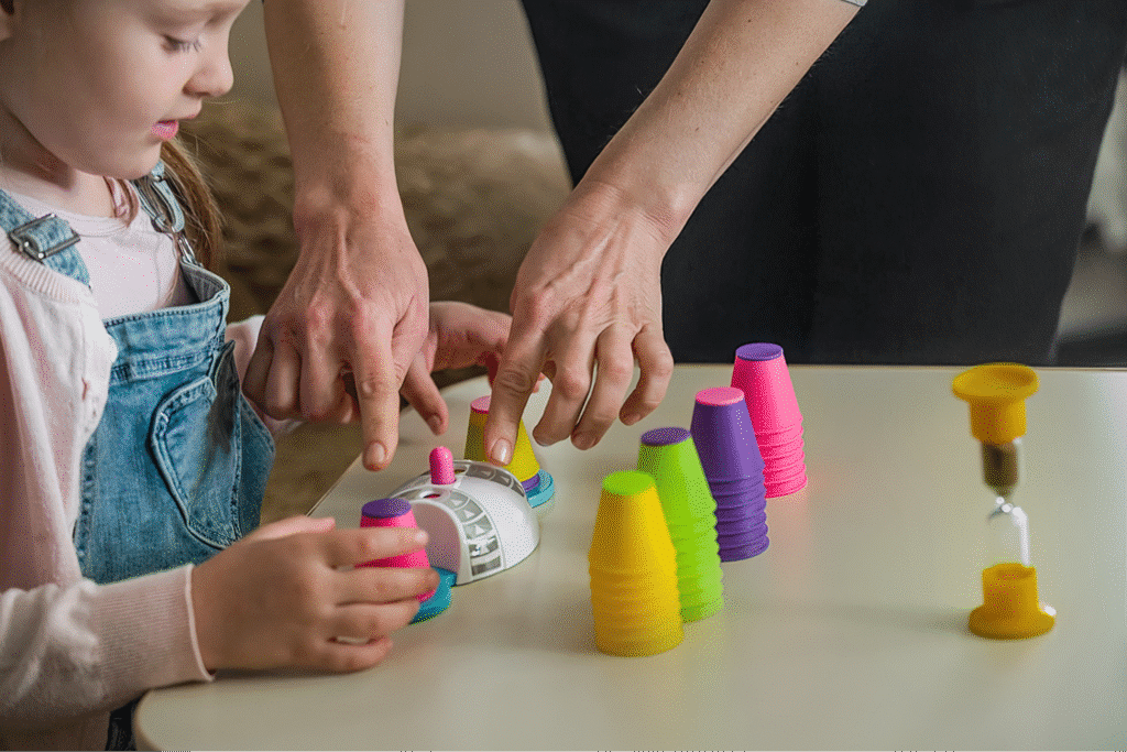 Child playing with colorful stacking cups, guided by an adult hand.