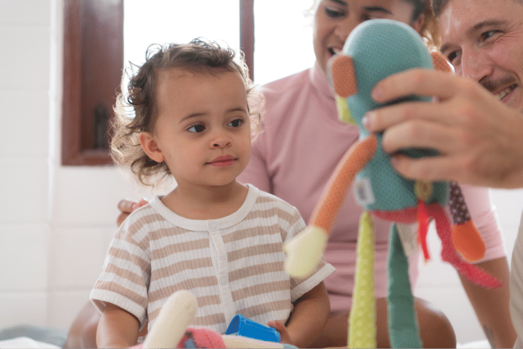 Child enjoys playful interaction with parents and colorful toys in a bright, cozy environment.
