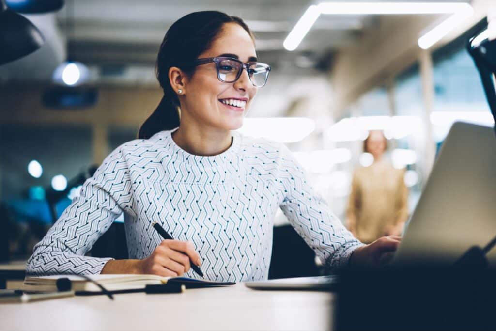Smiling woman working on a laptop in a modern office environment.