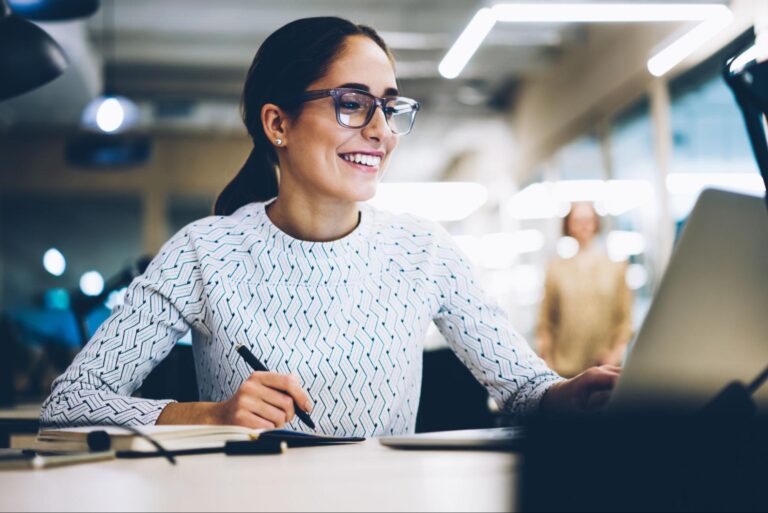 Smiling woman working on a laptop in a modern office environment.