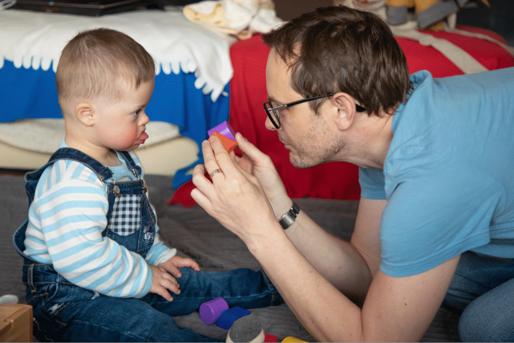 Father playing with toddler, encouraging creativity with colorful toys in a playful environment.
