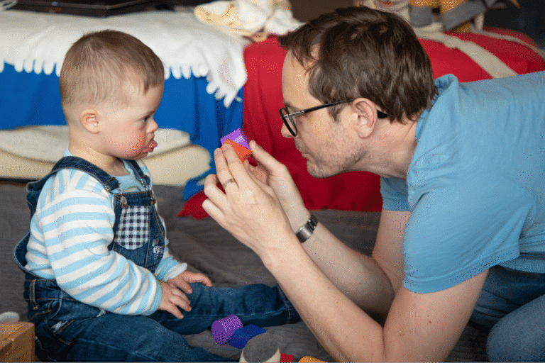 Father playing with toddler, encouraging creativity with colorful toys in a playful environment.