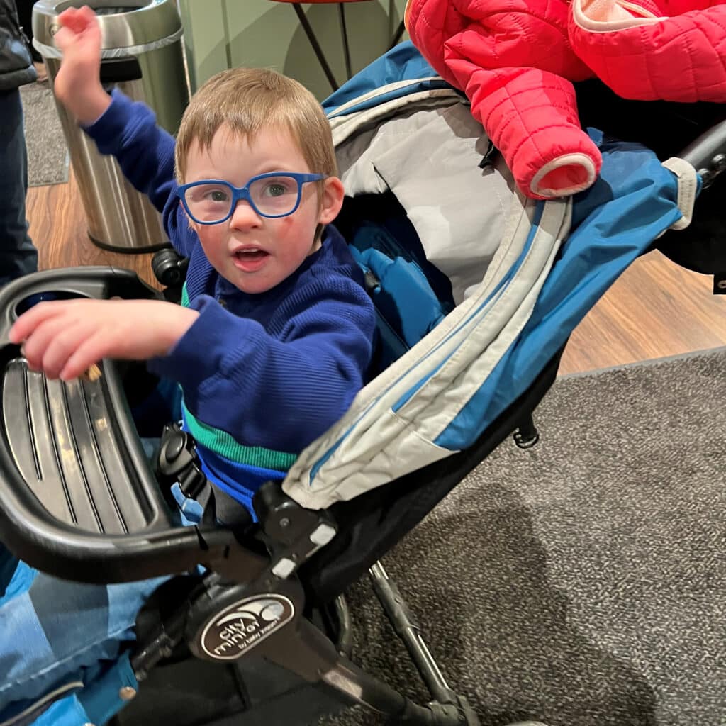 Happy toddler in a stroller, wearing glasses and a blue sweater, enjoying an outing.