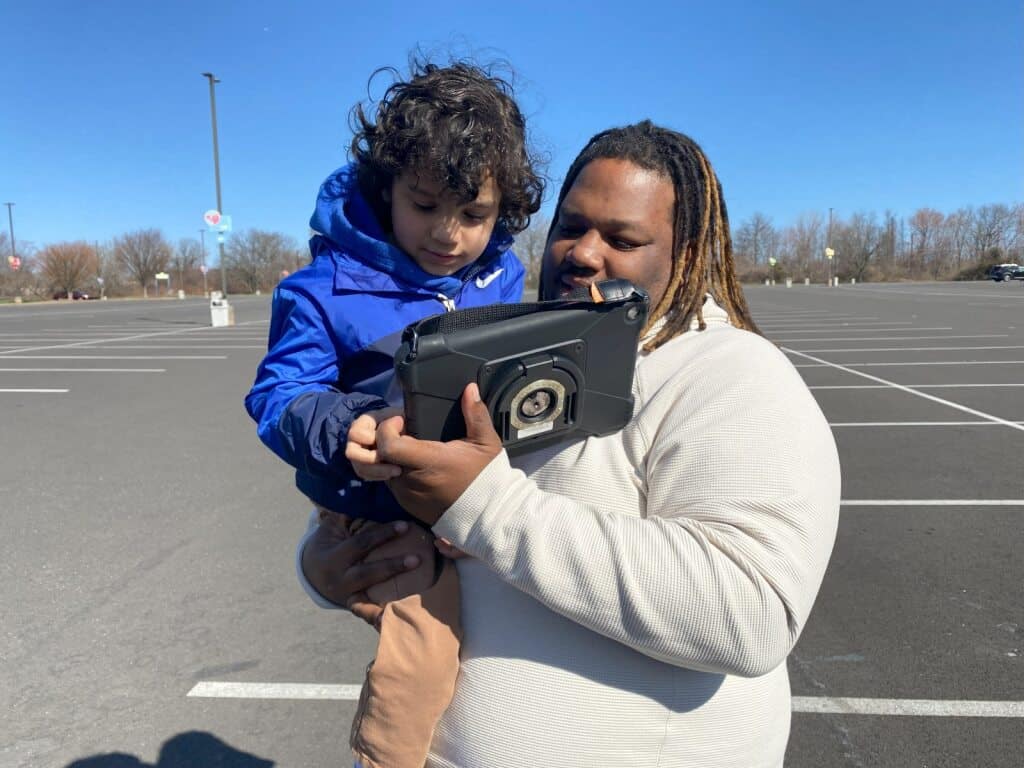 Parent and child exploring educational content on a tablet outdoors in the parking lot.