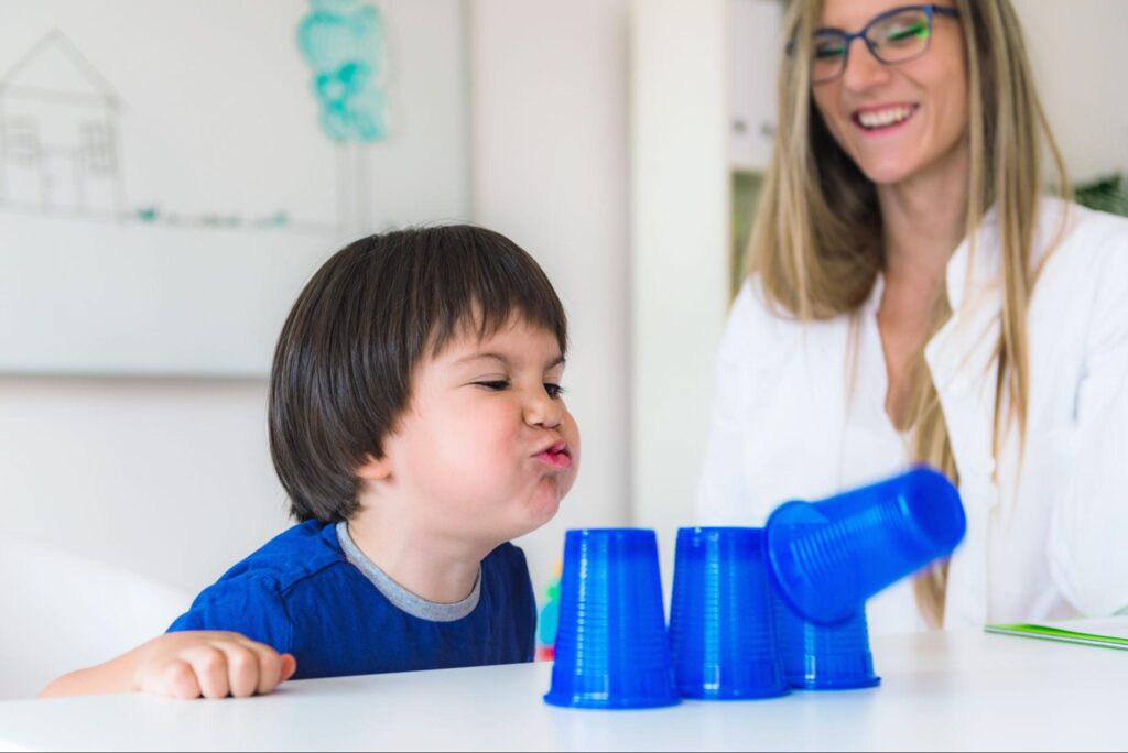 Child and speech language pathologist play with colorful cups in a bright, engaging learning environment.