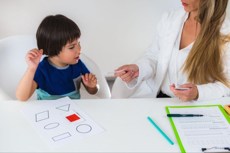 Child learns shapes with teacher, using colorful materials during a playful educational session.