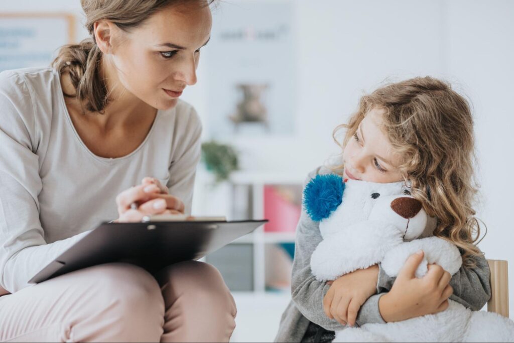 Child interacts with a caring SLP during a therapy session with a teddy bear.