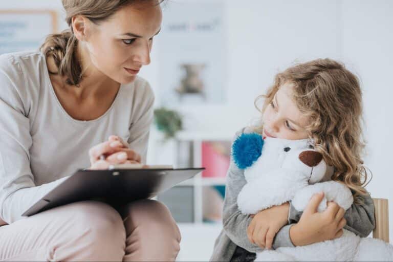 Child interacts with a caring SLP during a therapy session with a teddy bear.