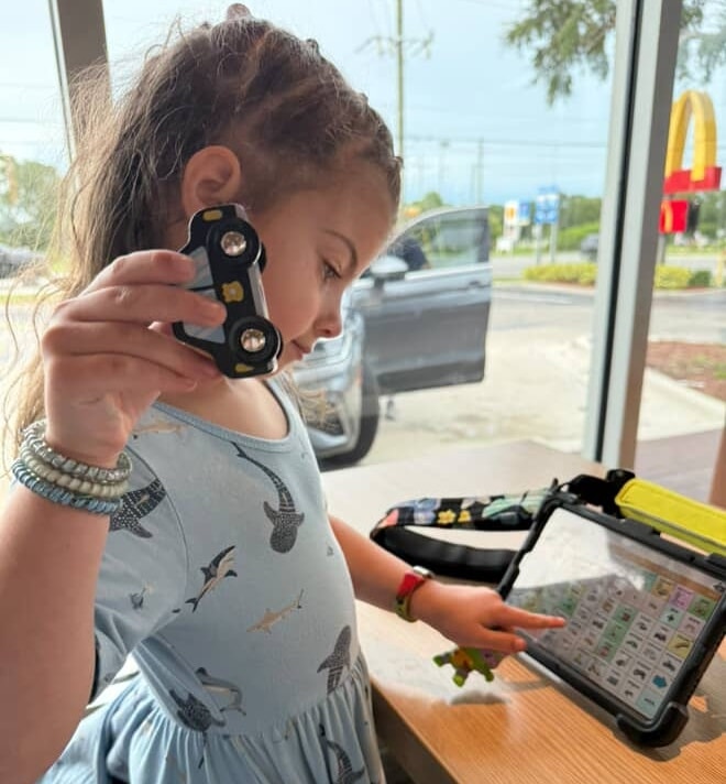 Child enjoying toy and tablet playtime at a restaurant table.