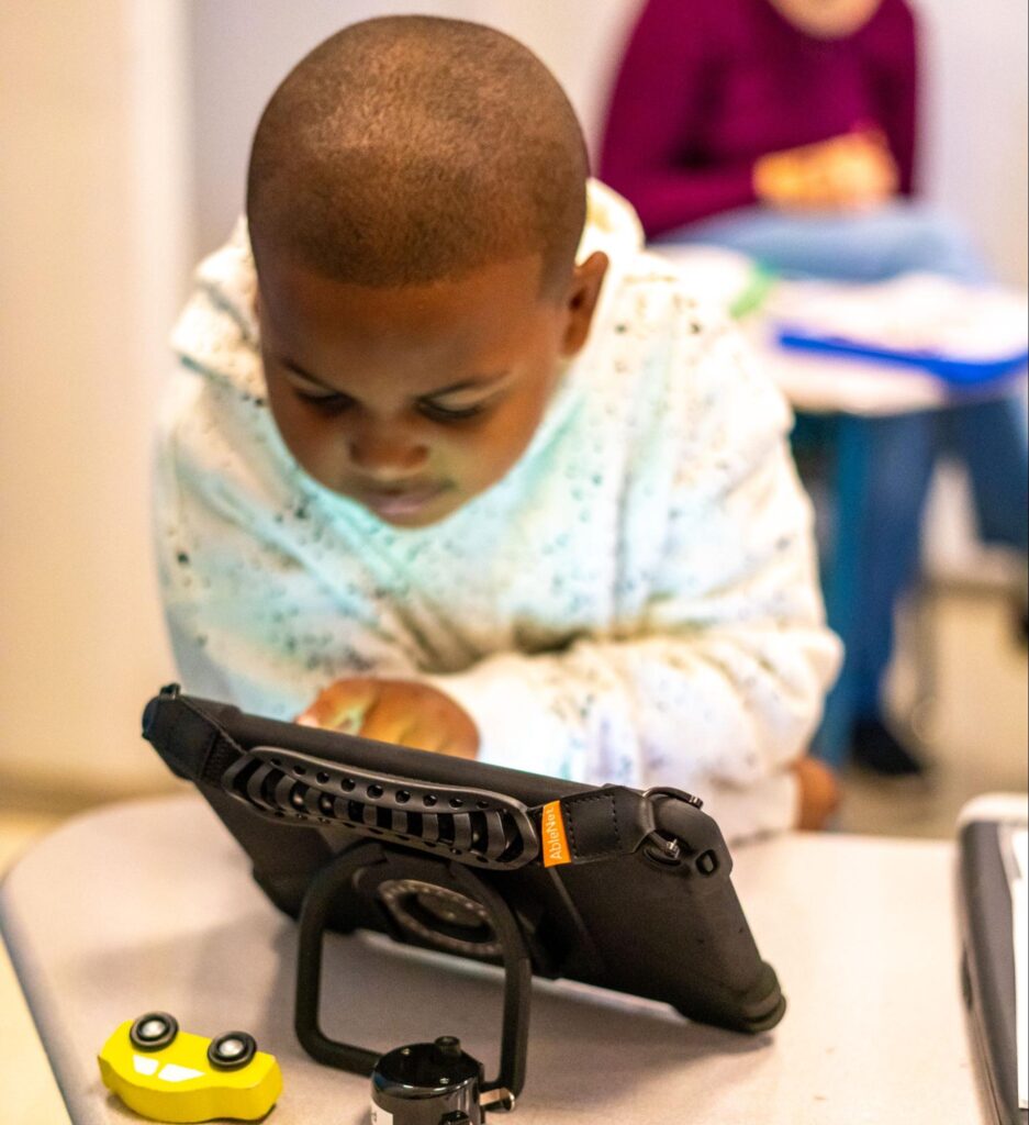 Child engaged with QuickTalker AAC device in a dynamic learning space.