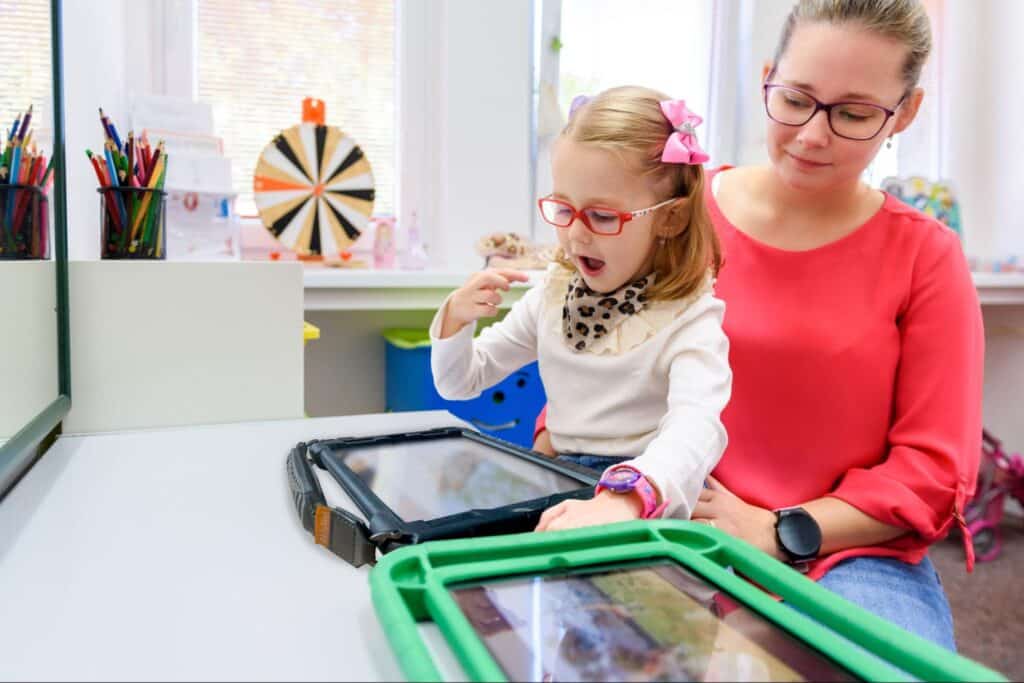 Child and SLP engaging in interactive learning using Quicktalker Freestyle AAC device in a bright classroom.