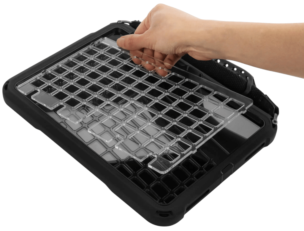 Hand lifting a clear plastic keyguard off a QuickTalker Freestyle tablet in a black protective case with a hand strap.