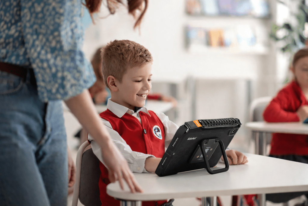 Student exploring technology with a Quicktalker Freestyle AAC tablet in an active classroom.