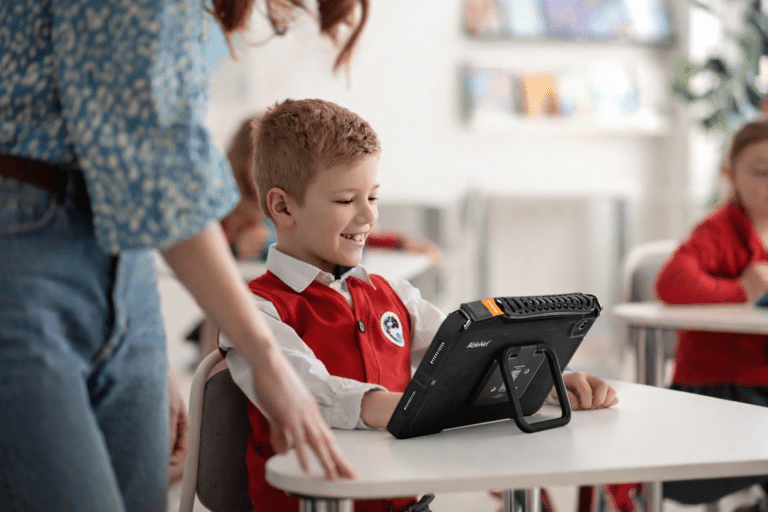 Student exploring technology with a Quicktalker Freestyle AAC tablet in an active classroom.