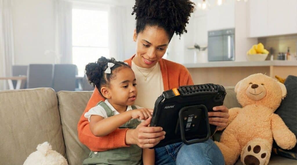 Mother and daughter enjoy quality time with an AAC device on the couch.