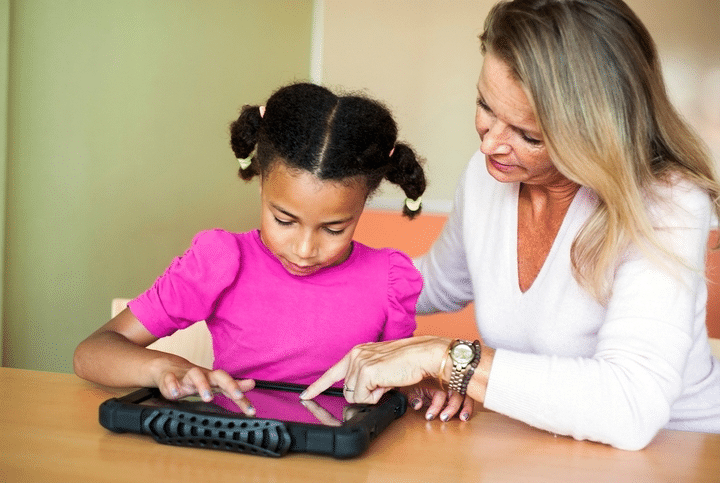 A woman helps a girl learn to use a Quicktalker Freestyle AAC device at home.