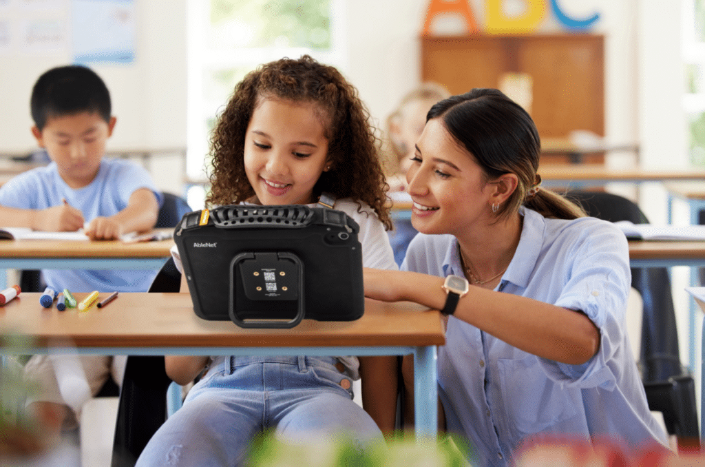 Teacher assists a student with their Quicktalker Freestyle AAC device in an interactive classroom setting.