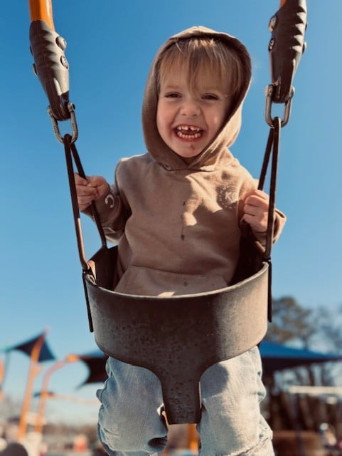 Smiling child enjoying a swing at the playground on a sunny day.
