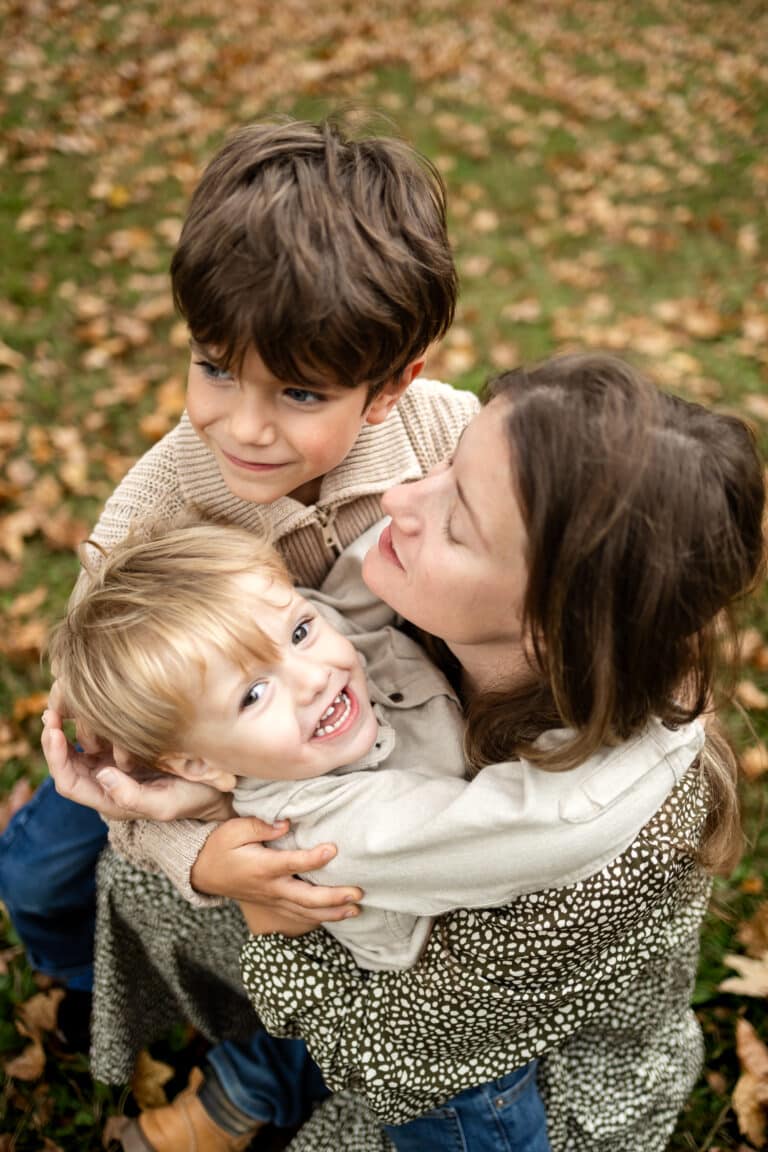 Joyful kids and mother enjoying autumn leaves outdoors, creating happy family moments.