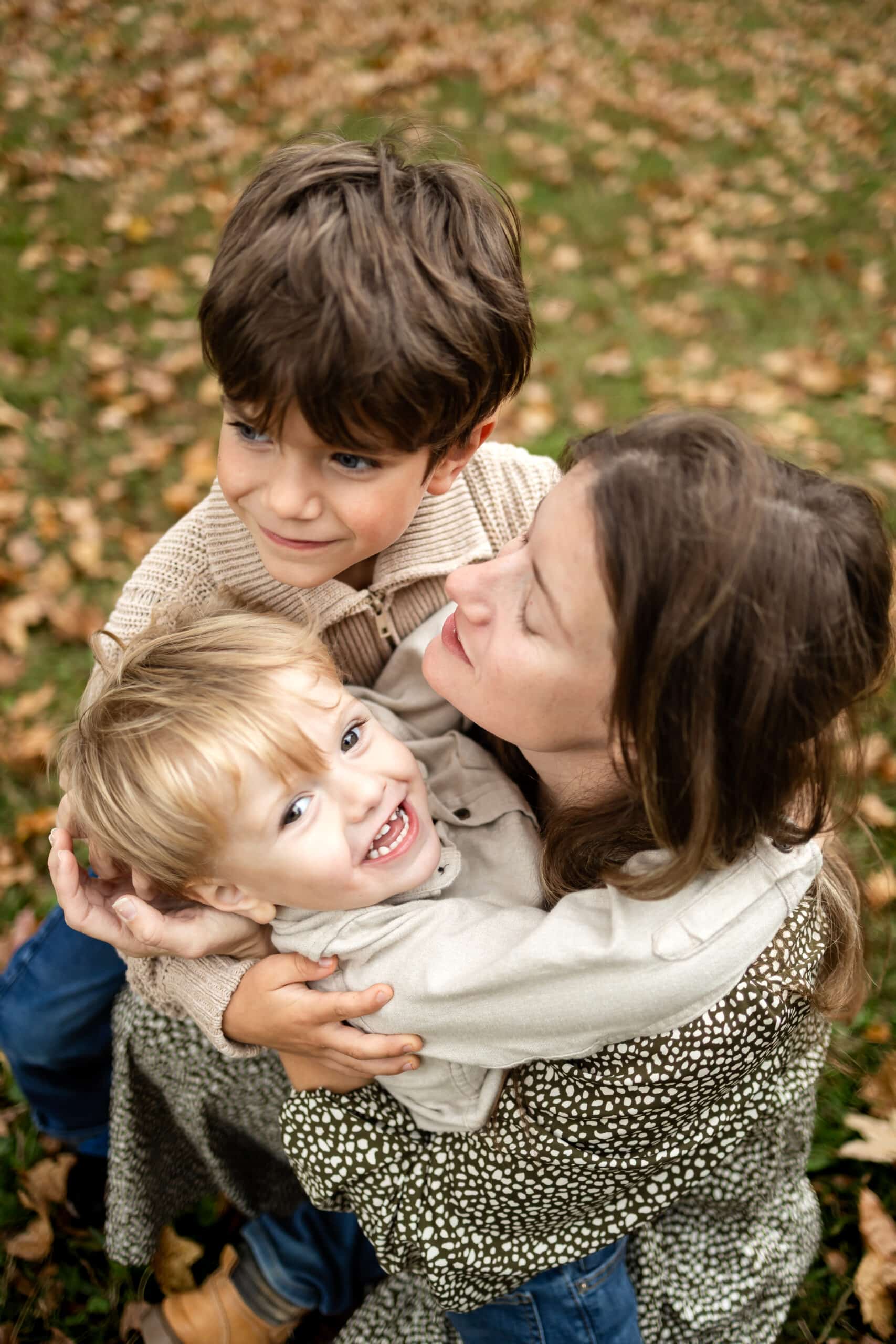 Joyful kids and mother enjoying autumn leaves outdoors, creating happy family moments.
