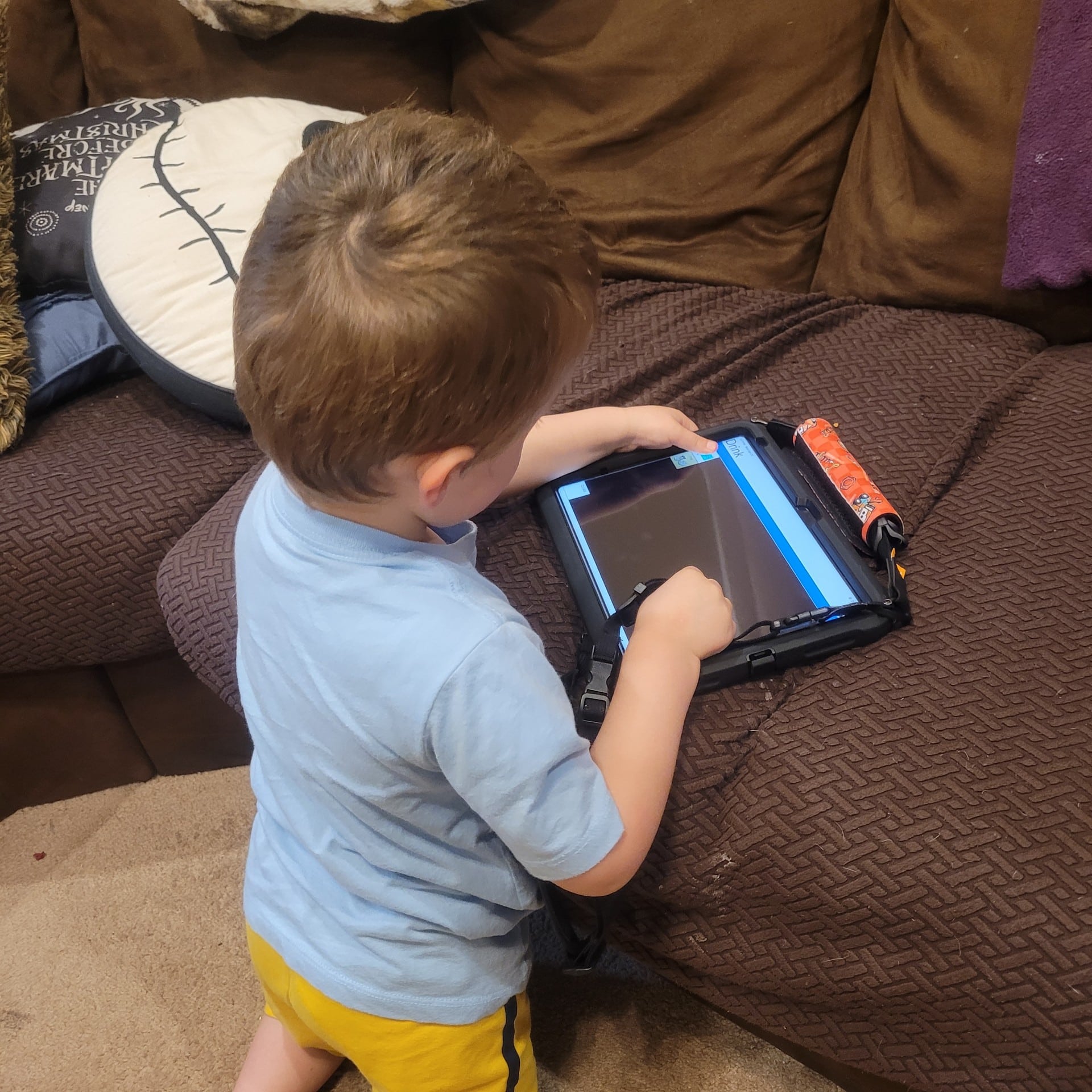 Toddler engaging with a tablet for learning and educational play on a couch.