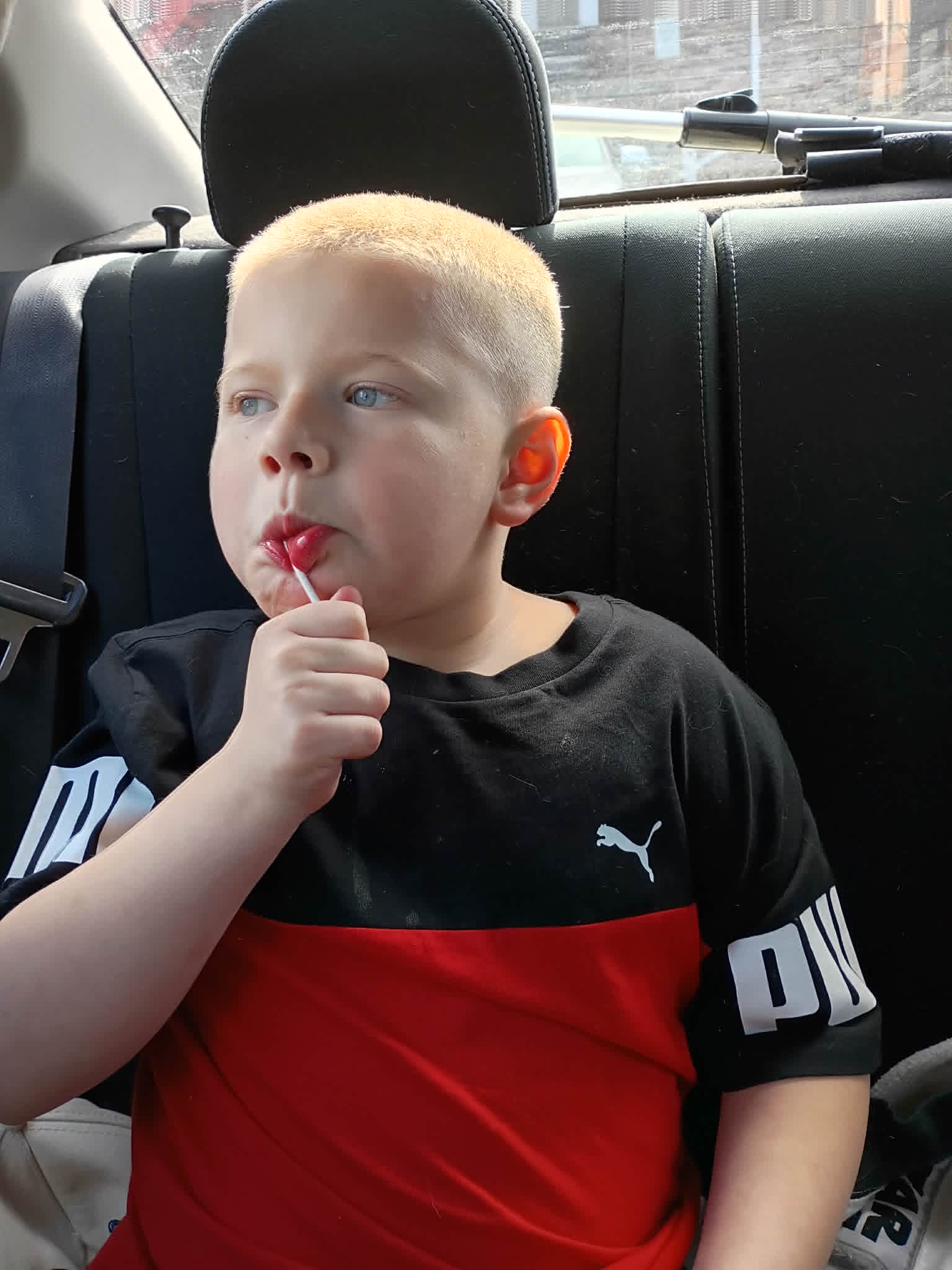 Boy in a car enjoys a lollipop, showcasing ablefamilies moments of joy.