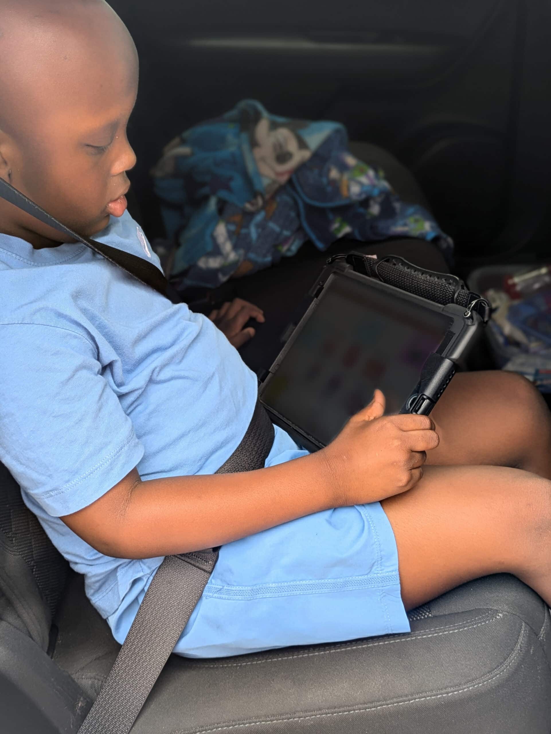 Child in a seatbelt using a tablet during a family car ride.
