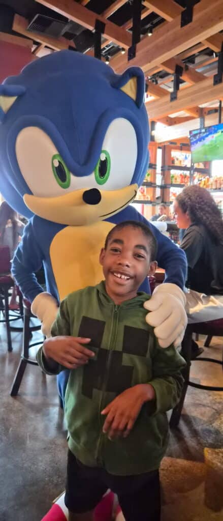 A child smiles joyfully with Sonic, enjoying a fun family outing.