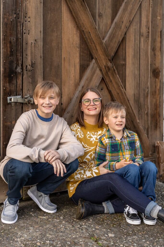 Dana sits with her sons, Jackson and Logan, in front of a rustic wooden barn door.