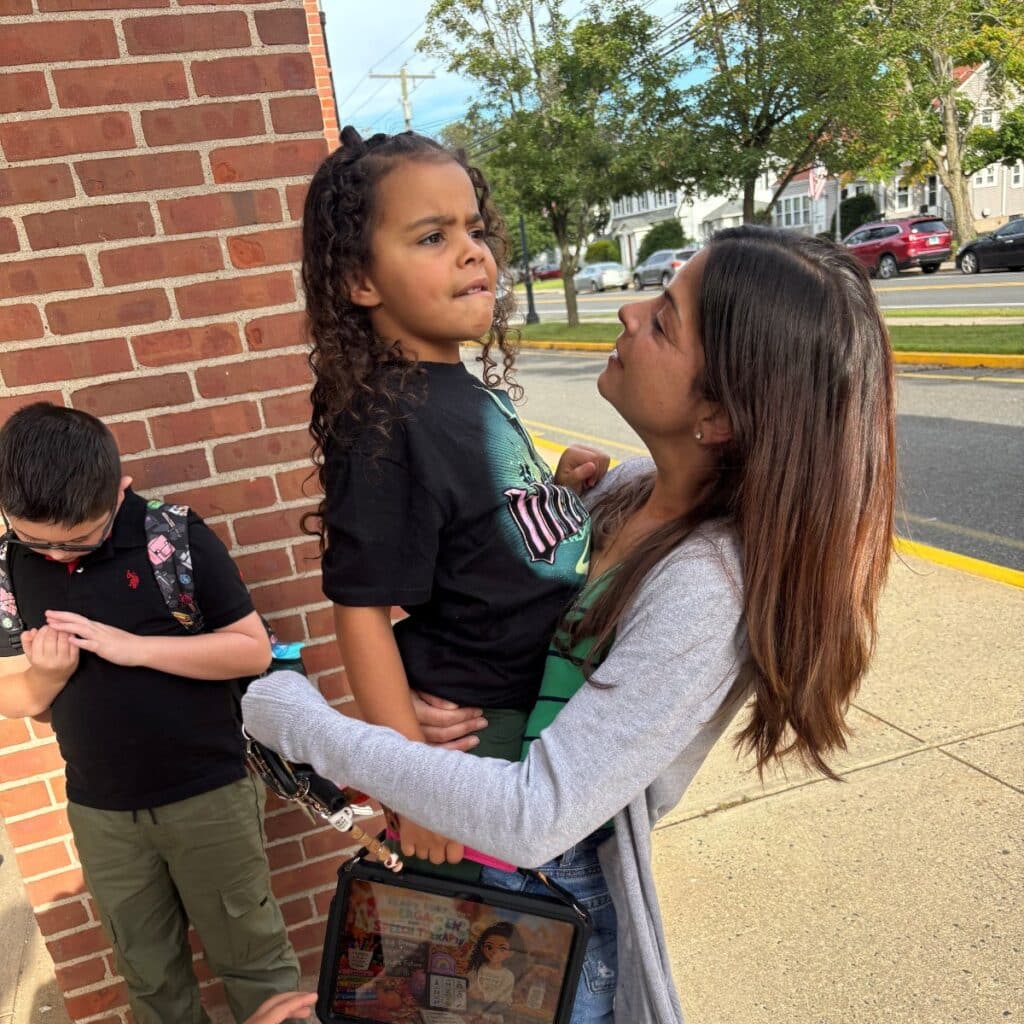 Shayna holding her daughter Aria outside, with Aria's QuickTalker Freestyle AAC device at her side