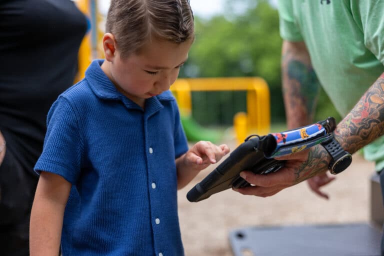 Child uses Quicktalker device at playground for interactive play and communication.