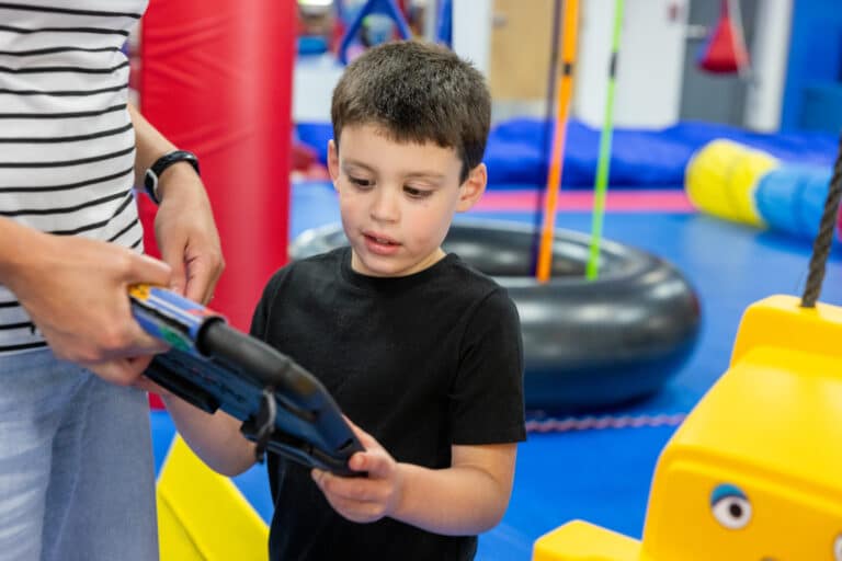 Child engages with Quicktalker Freestyle device in an active gym setting.