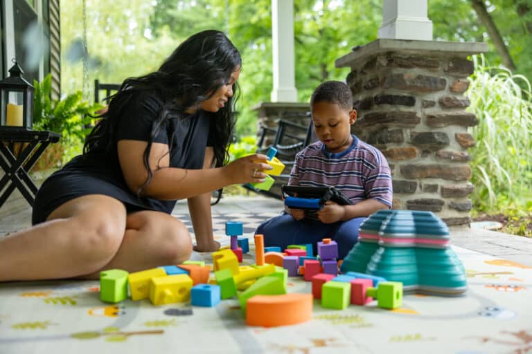 Family enjoys outdoor playtime at home with colorful blocks and the Quicktalker Freestyle device.