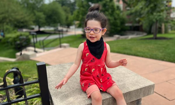 Smiling child in a red dress enjoys playing outside in a park.