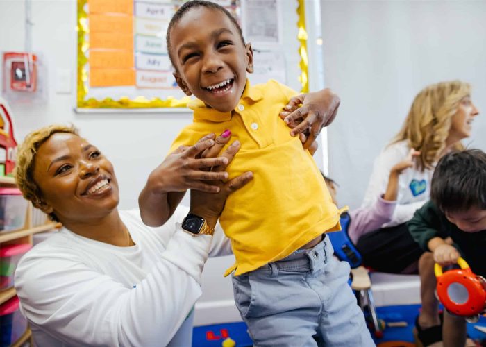 Joyful child laughing in classroom, embraced by caregiver at Ann Storck Center.