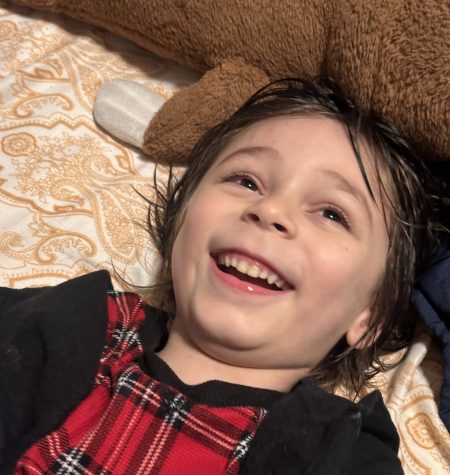 A cheerful child laughing joyfully on a cozy bed with a stuffed animal.