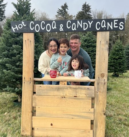 Family enjoying hot cocoa and candy canes at a festive outdoor stand.